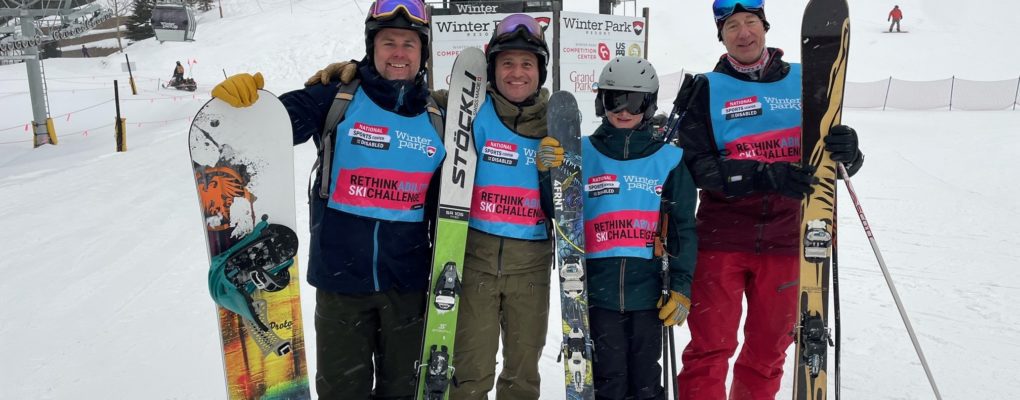 Four Challengers take on the RethinkAbility Ski Challenge! From left to right, a snowboarder and three skiers stand on a Winter Park ski run with their arms around each other.